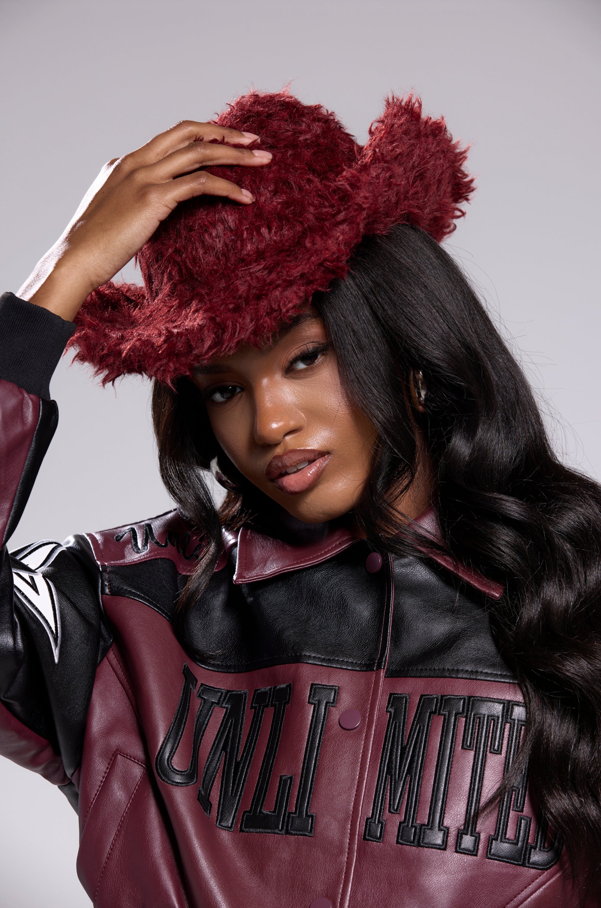 A woman confidently adjusts her FOR THE VIBES FAUX FUR COWBOY HAT while wearing a burgundy and black leather "UNLIMITED" jacket, perfectly capturing bold western flair. 1