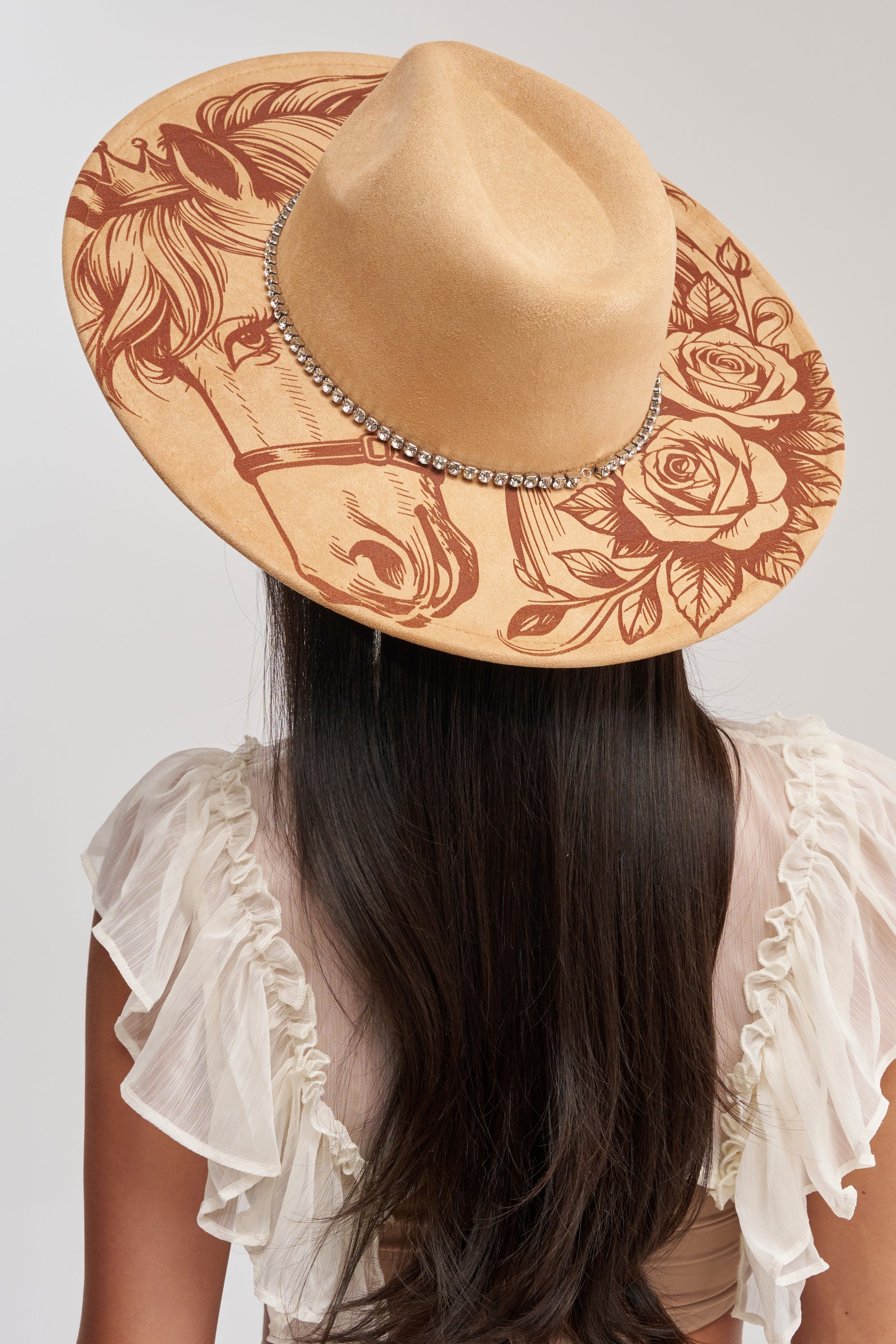 A woman with long dark hair wears the HORSE GIRL 4 EVA BRIM HAT featuring an intricate horse, roses, and leaves design with a beaded band, paired with a ruffled, sheer white top.