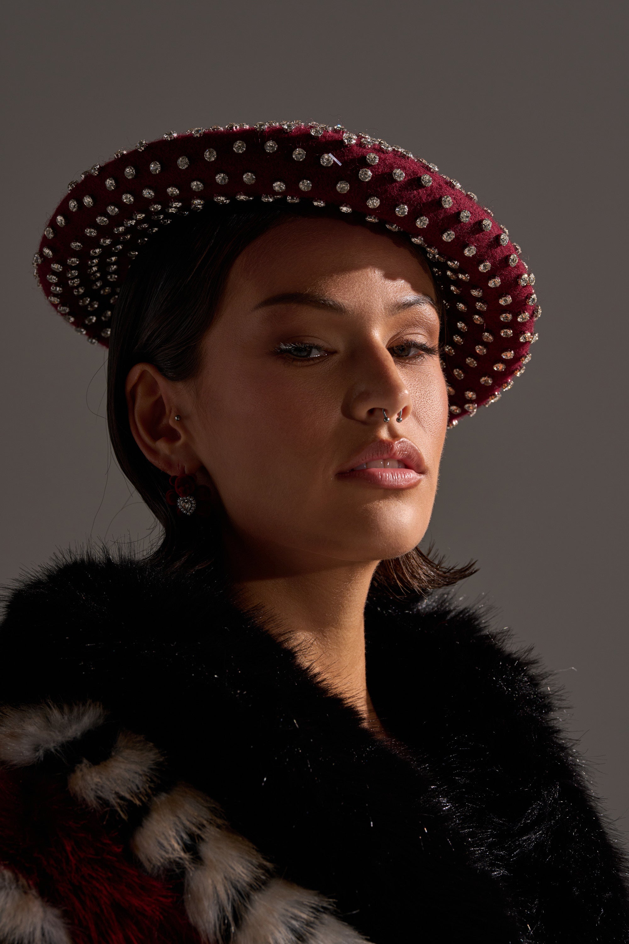 A woman confidently faces the camera wearing THE REAL RELATE EMBELLISHED BERET and a black fur coat against a plain background. 0