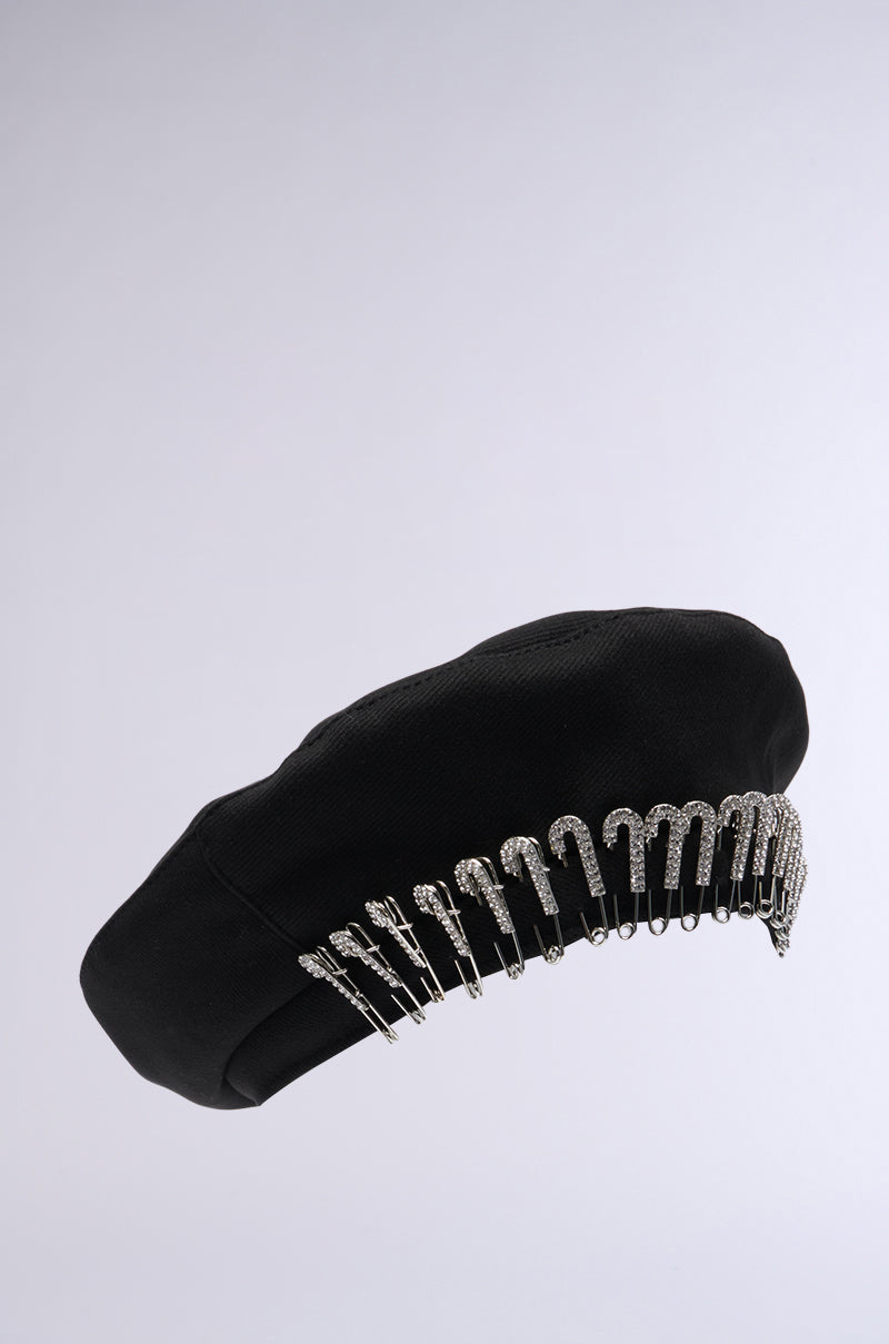 The SAFETY FIRST BERET is a stylish black AKIRA Label beret adorned with a row of silver safety pins around its edge, each pin decorated with small crystals, set against a plain background. 3