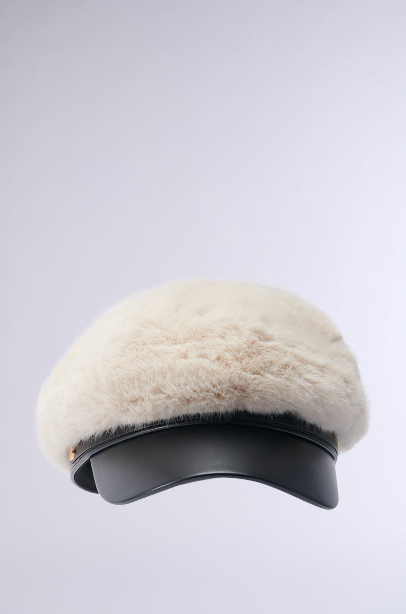 The IN THE CITY FUR BRIM HAT features a chic design with a fluffy, cream-colored faux fur top and a shiny black visor, elegantly contrasted against a simple gray background.
