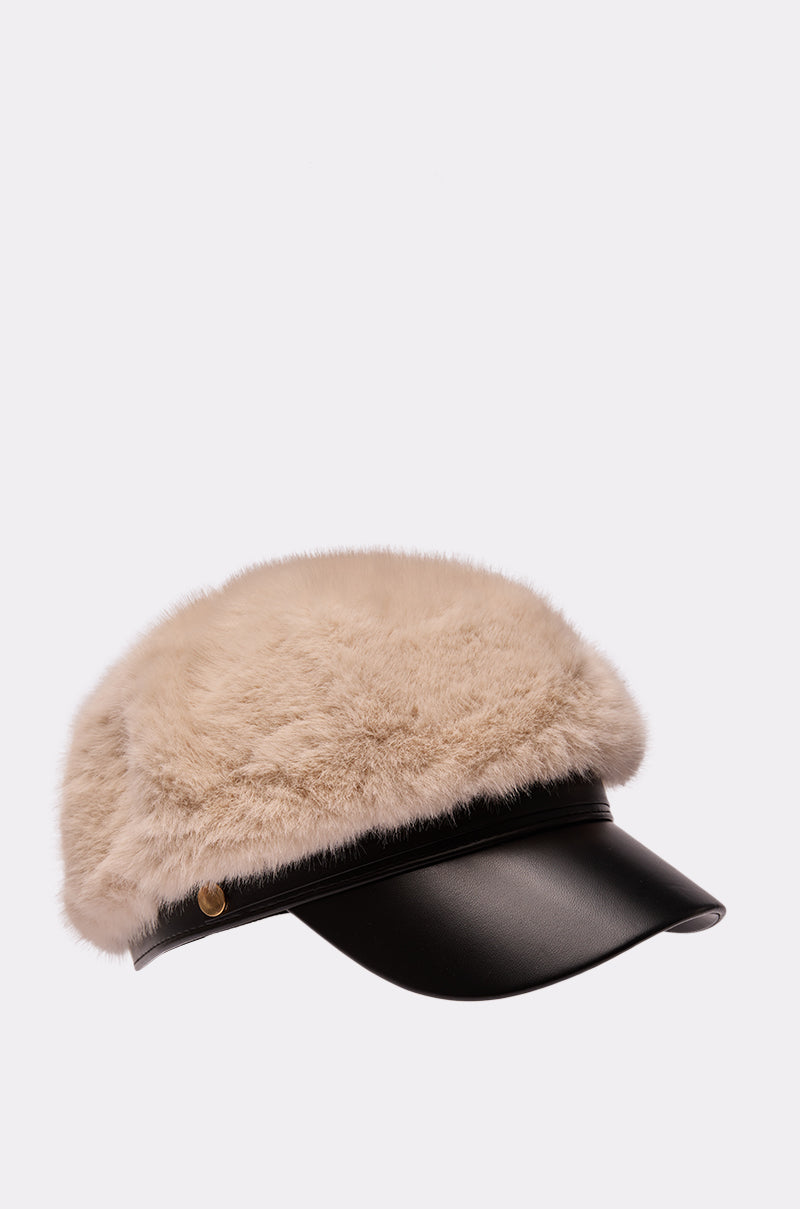The IN THE CITY FUR BRIM HAT is a stylish fisherman cap with a black leather brim, fluffy beige faux fur crown, and a small gold side button, shown against a plain light gray background.