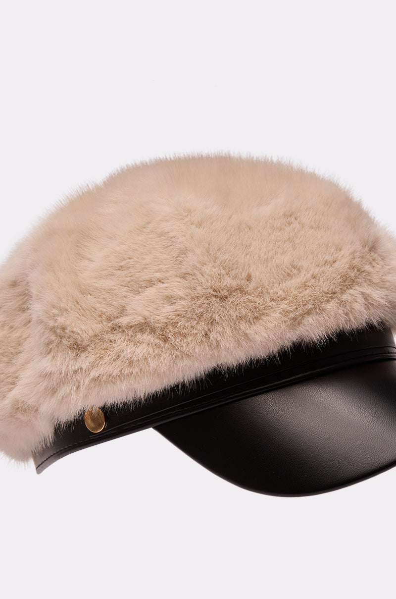 The IN THE CITY FUR BRIM HAT is a black leather fisherman cap with a wide, plush beige faux fur brim covering the top and sides, finished with a gold button detail.