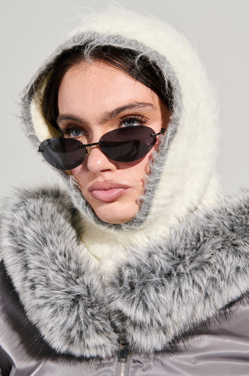 A person in sunglasses, the COZY SEASON ULTRA LUXE SNOOD in fluffy white, and a coat with a gray fur collar. The plain background highlights the stylish winter ensemble.