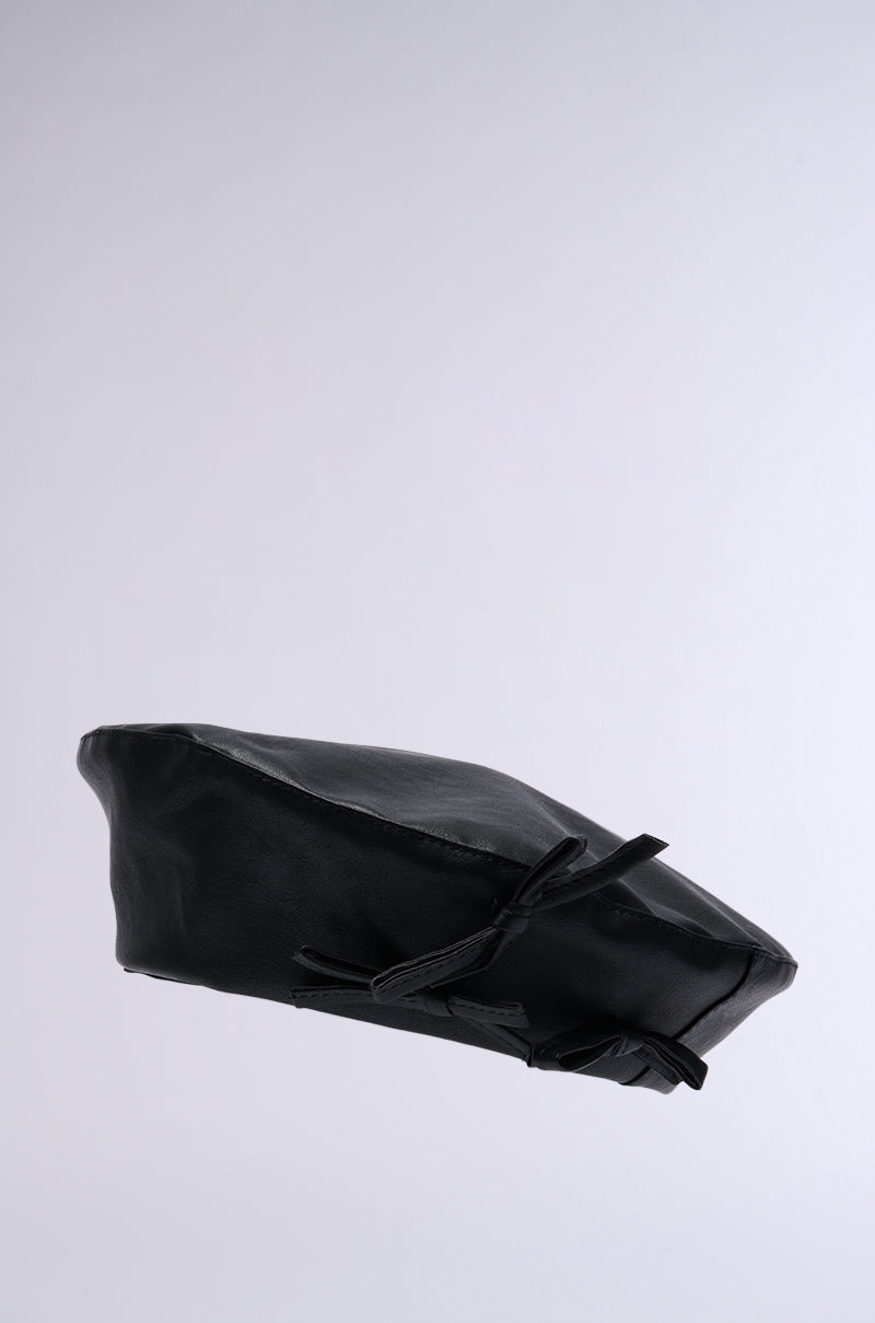 An image of the PRETTY IN PU BOW BERET, crafted from luxurious black faux leather and featuring a knot tied detail on the side, along with adjustable drawstrings for a perfect fit. The beret is displayed against a plain light grey background, showcasing its sleek texture and stylish design. 3