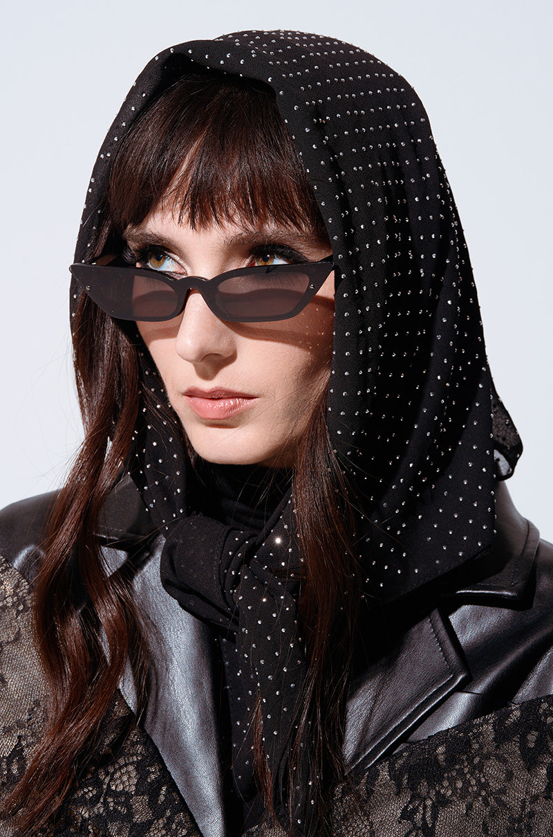 A person with long brown hair wears black cat-eye sunglasses and a GLAM LIFE SCARF embellished with petite silver rhinestones. They also wear a black leather jacket over a black lace top. The background is plain white.
