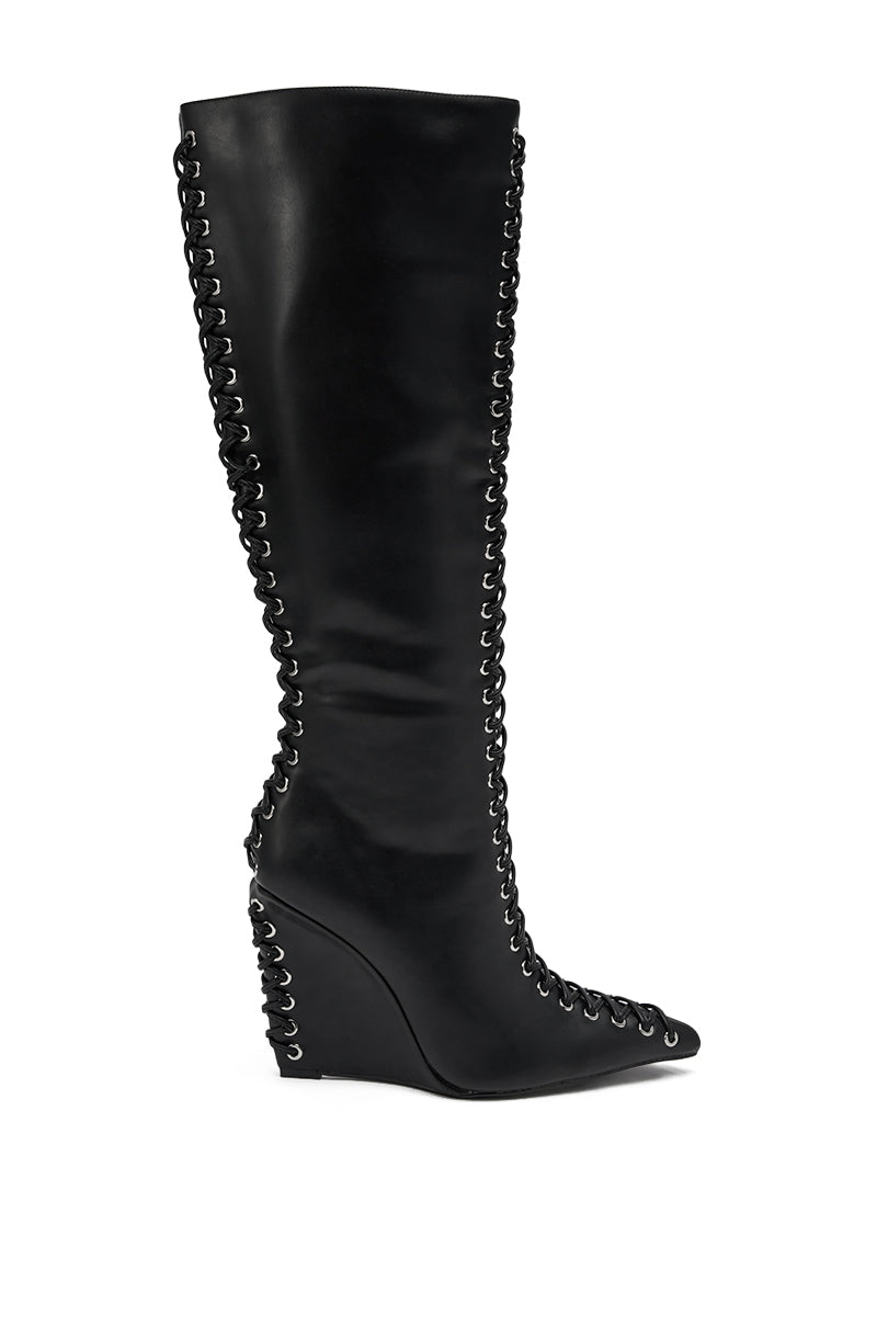 The AZALEA WANG THAUMUS BLACK LACE UP WEDGE BOOT features black faux leather, decorative silver eyelets, and front-and-side lacing, shown in side profile against a white background. 5