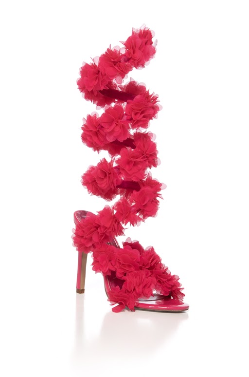A vibrant pink AZALEA WANG THEODOSIA Stiletto Sandal featuring a bold spiral strap with large layered floral appliques that wrap up the leg, set against a plain white background.