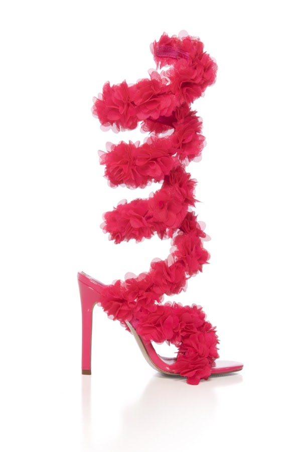 The AZALEA WANG THEODOSIA Pink Stiletto Sandal features a vibrant pink hue, a dramatic spiral strap with large floral appliques wrapping up the leg, and is shown against a white background.