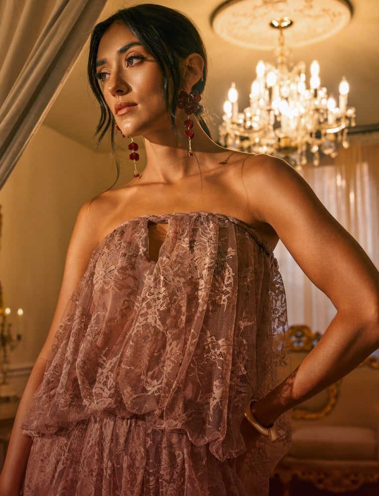 A woman wearing a strapless dusty rose lace dress in an elegant room with a chandelier in the background.