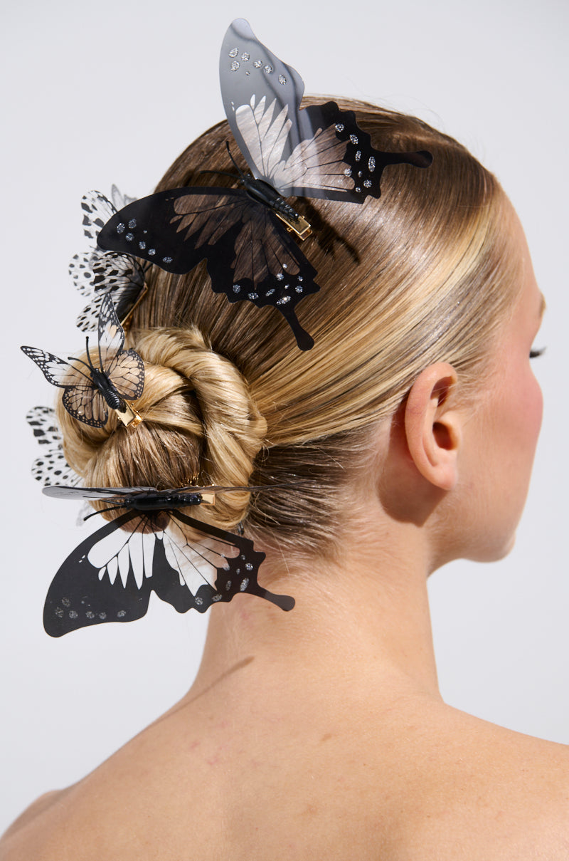 A woman with blonde hair styled in an elegant bun is adorned with whimsical accessories, featuring the LET ME FLY AWAY HAIR CLIP SET with decorative black and white butterflies.