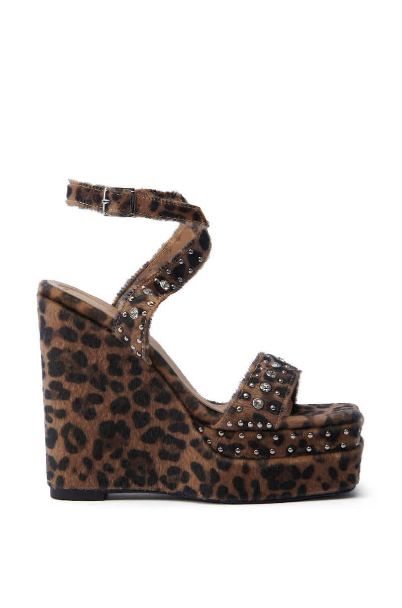 The AZALEA WANG TIBIL LEOPARD WEDGE SANDAL features a platform sole, ankle strap, metallic studs, open toe design, textured fabric detail, and high platform heel.