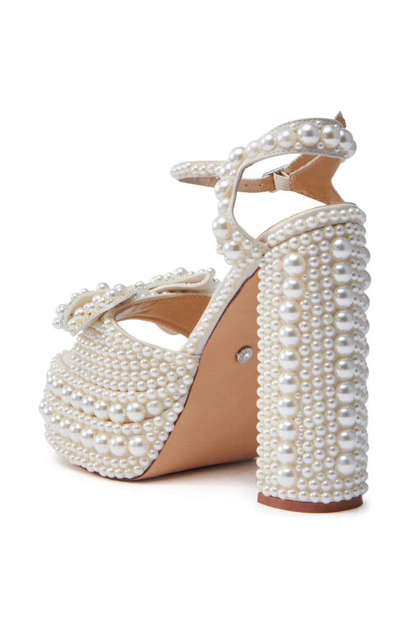 The AZALEA WANG TIMEA WHITE CHUNKY SANDAL is a high-heeled platform with pearl-adorned mega-chunky heel and ankle strap. It features a comfort cushion insole for all-day wear, complemented by a classic tan-colored sole.