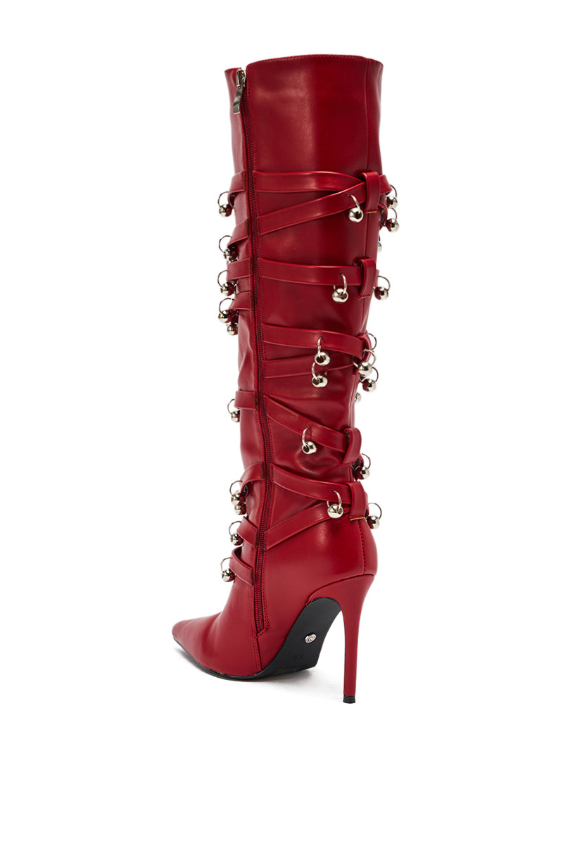 The AZALEA WANG TIMPANI Red Western Fringe Stiletto Boot is a tall boot featuring a pointed toe, side zipper, and decorative crisscross laces with silver studs and rings running up the back.