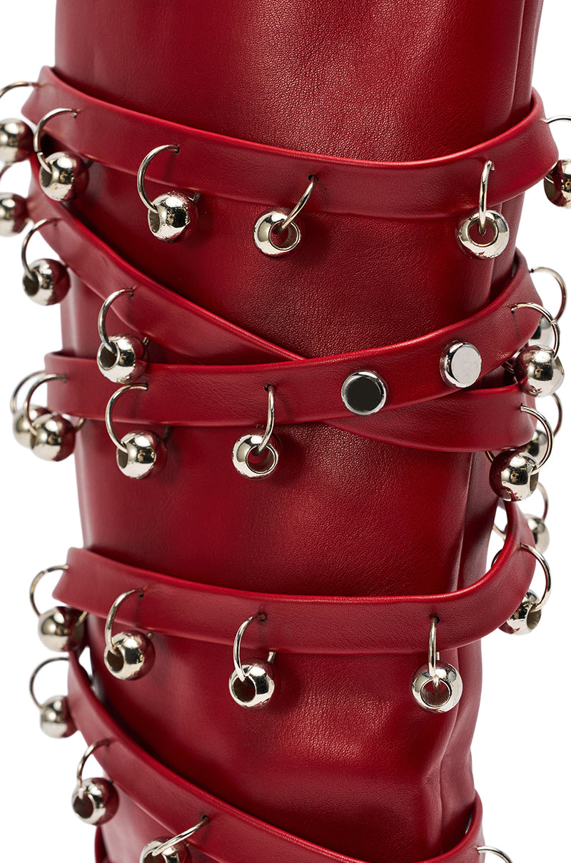 Close-up of the AZALEA WANG TIMPANI RED WESTERN FRINGE STILETTO BOOT's red leather, wrapped with matching straps and silver jingle bells, inspired by bold western style for a festive look.