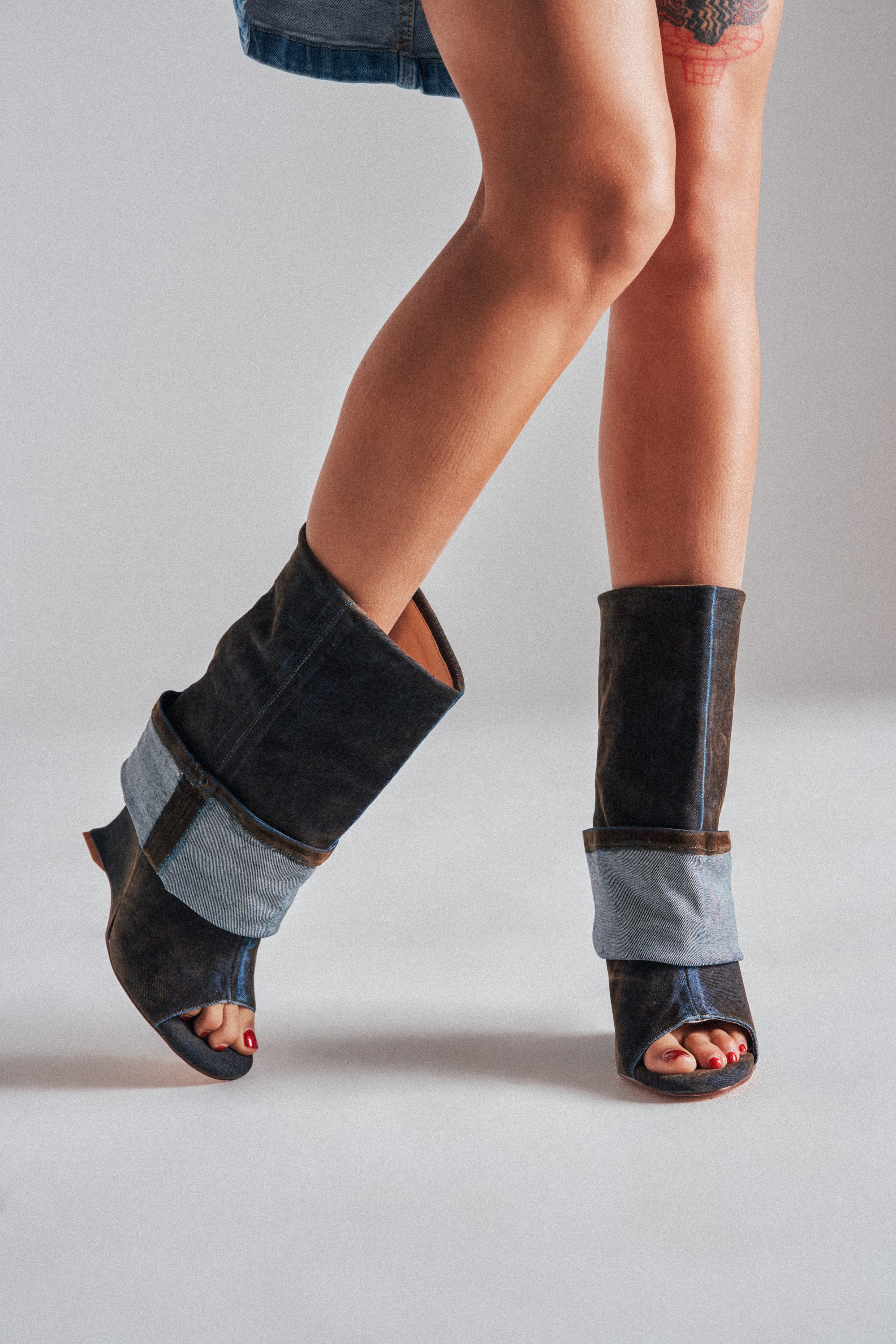 A person with bare legs wears denim shorts and the AZALEA WANG TIN BROWN CUFFED WEDGE BOOTIE, featuring dark leather and light blue denim details, standing against a plain light background.