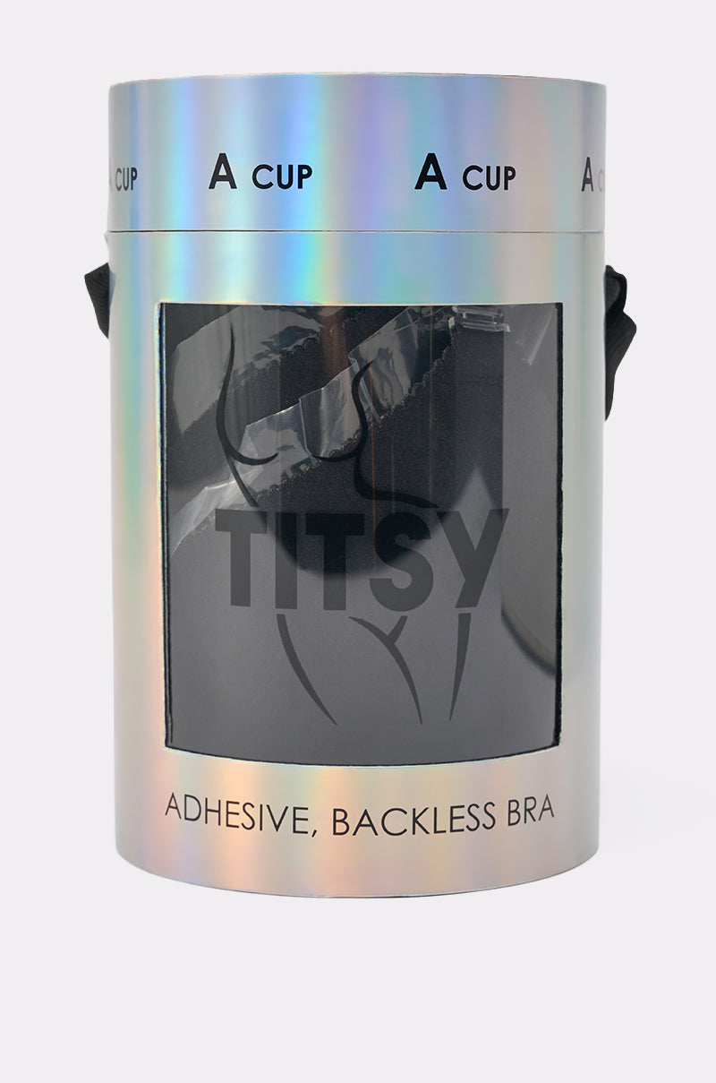 A holographic cylindrical package labeled "A CUP" and "TITSY ADHESIVE BRA" displays a strapless, backless adhesive bra through a front window. The shiny packaging features black text, a simple illustration, and highlights the invisible bra design. 4