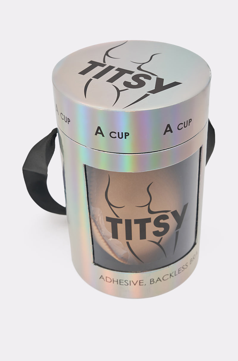 A cylindrical, iridescent box labeled "TITSY ADHESIVE BRA IN NUDE," with a black handle and transparent window revealing the adhesive bra inside, designed to provide invisible support. 4