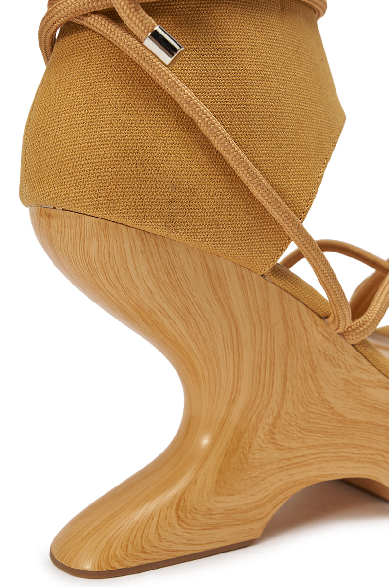 Close-up of the AZALEA WANG TIZIANO TAN GLADIATOR WEDGE SANDAL, featuring a tan fabric upper, sculptural wood-grain wedge heel, and thin matching laces that wrap elegantly around the ankle. 7