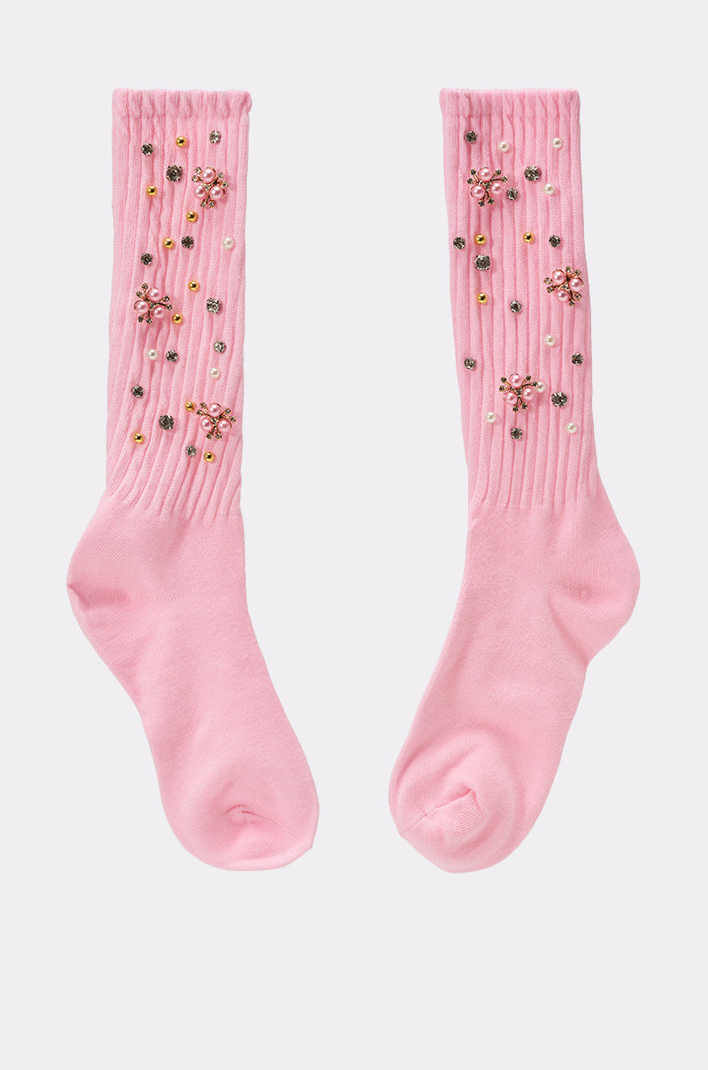 The EMBELLISH ME SOCKS are pink crew socks with ribbed cuffs, adorned with colorful beads and small floral embellishments scattered across the top. 3