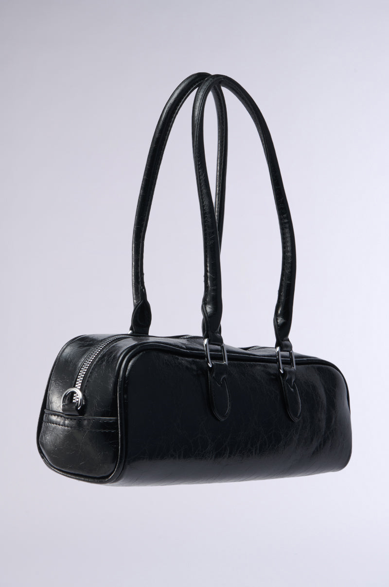 The BADDIE BARREL BAG is a black faux leather handbag with two long handles, silver buckles, a side zipper, and a detachable shoulder strap, displayed on a plain light gray background.