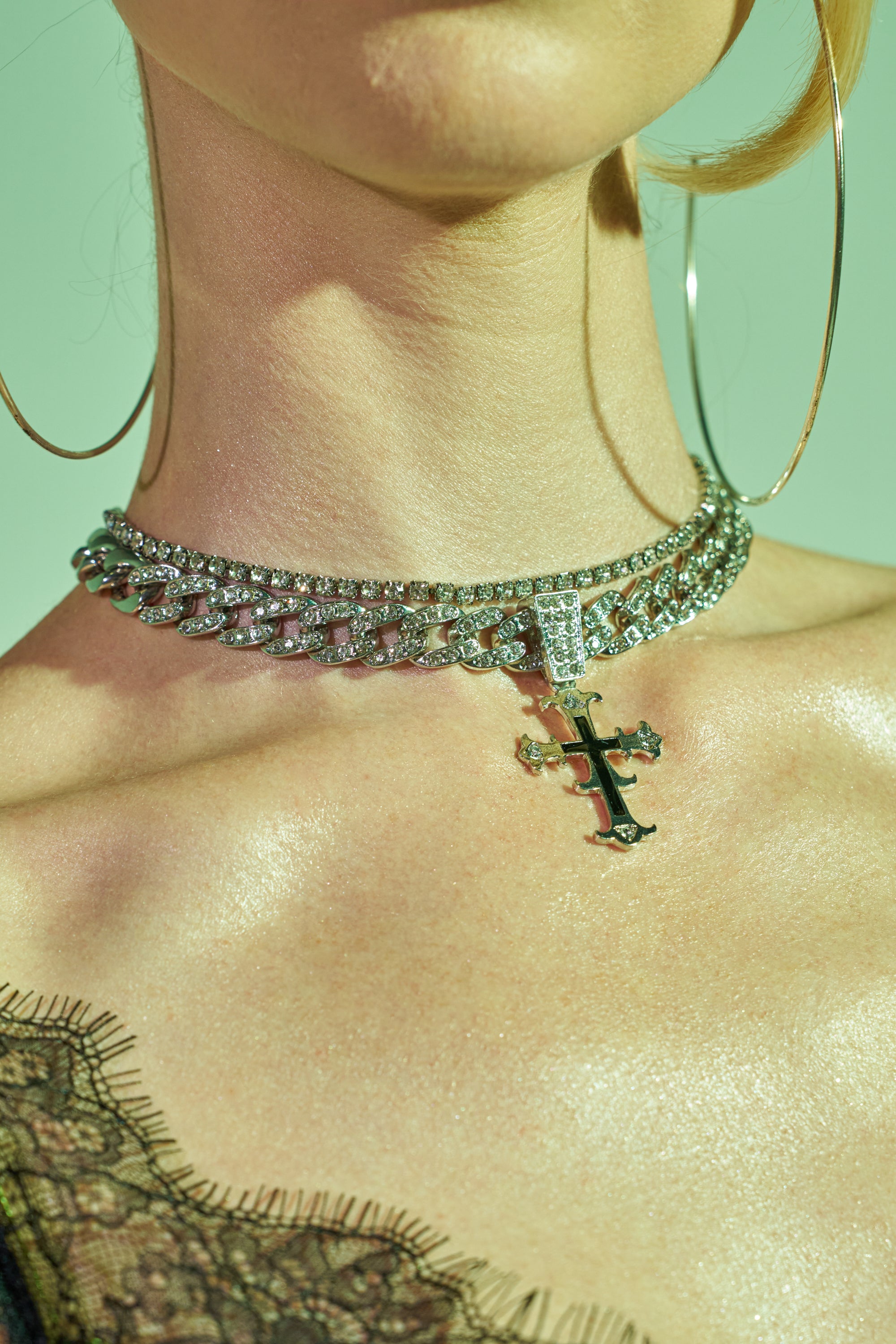 Close-up of a person wearing large hoop earrings and the ON INSTA NECKLACE, a layered piece featuring a tennis chain and cross pendant, with part of a lacy black garment visible on their shoulder.