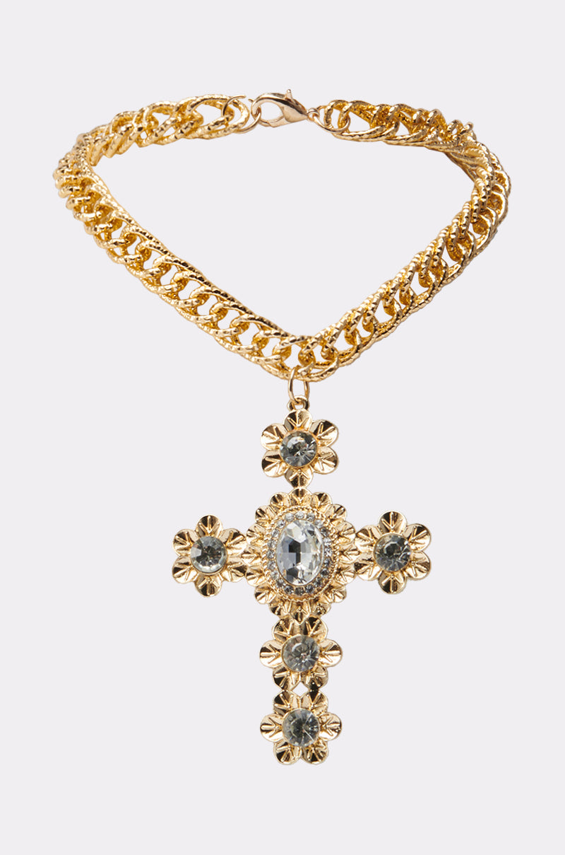 The KIMMY NECKLACE is a gold chain featuring an oversized cross pendant with six clear gemstones set in flower-shaped gold, shown on a simple light background. 2