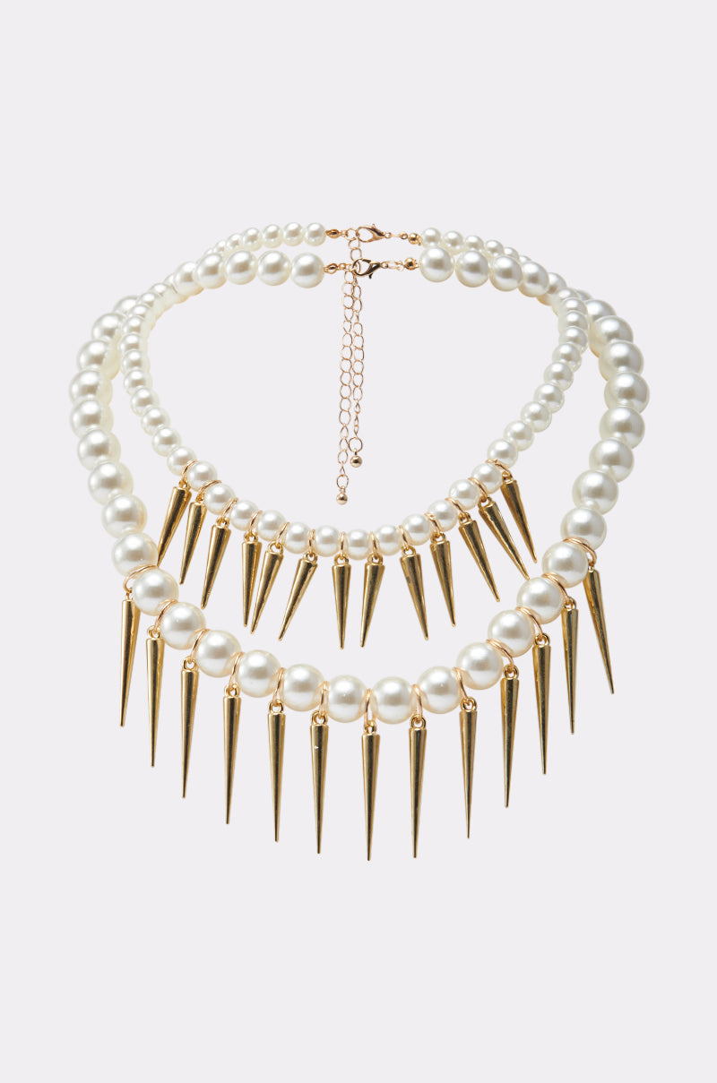 The BITE ME NECKLACE features two layers of large faux pearls; the lower strand is accented with evenly spaced spike embellishments, shown against a simple light background.