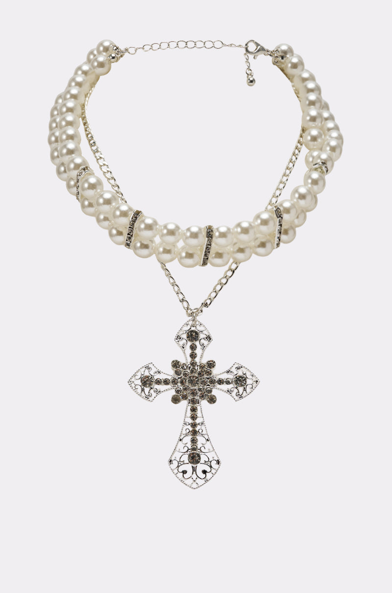 The PURE CROSS NECKLACE features a double-strand pearl choker with silver spacers and an ornate rhinestone cross pendant, set against a plain light background. 0