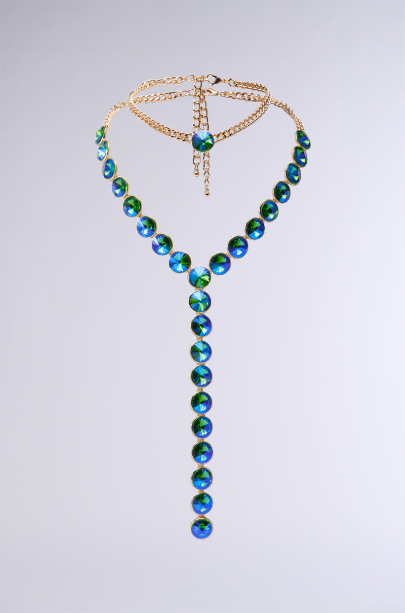 The JASMINE LONG NECKLACE is a breathtaking gold chain with a Y-shape design, featuring circular gemstones in shades of blue and green. Its bejeweled centerpiece stands out beautifully, with the gems continuing in a vertical line against a plain backdrop for an elegant appearance.