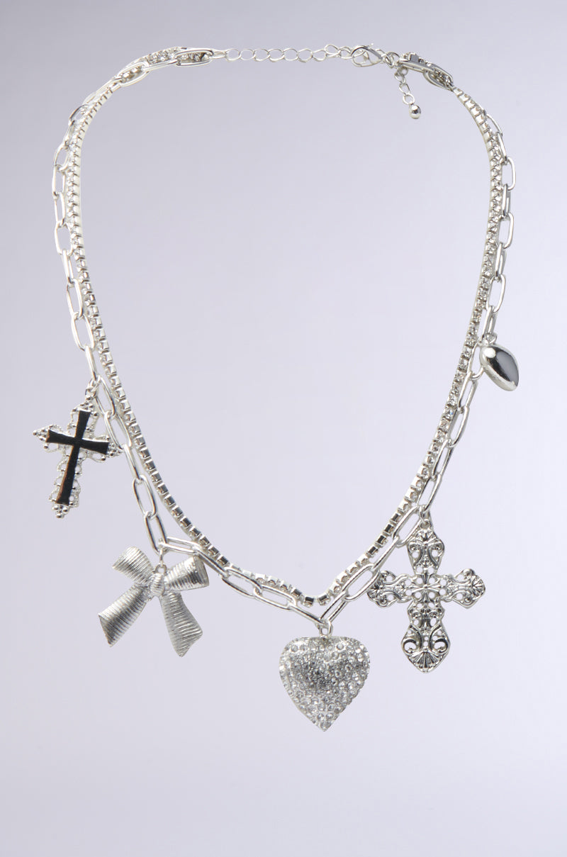 The IT GIRL SILVER NECKLACE, featuring a blend of links and rectangular segments, is adorned with rhinestone charms: a black cross, a shimmering heart, a silver rose, and a jeweled cross.