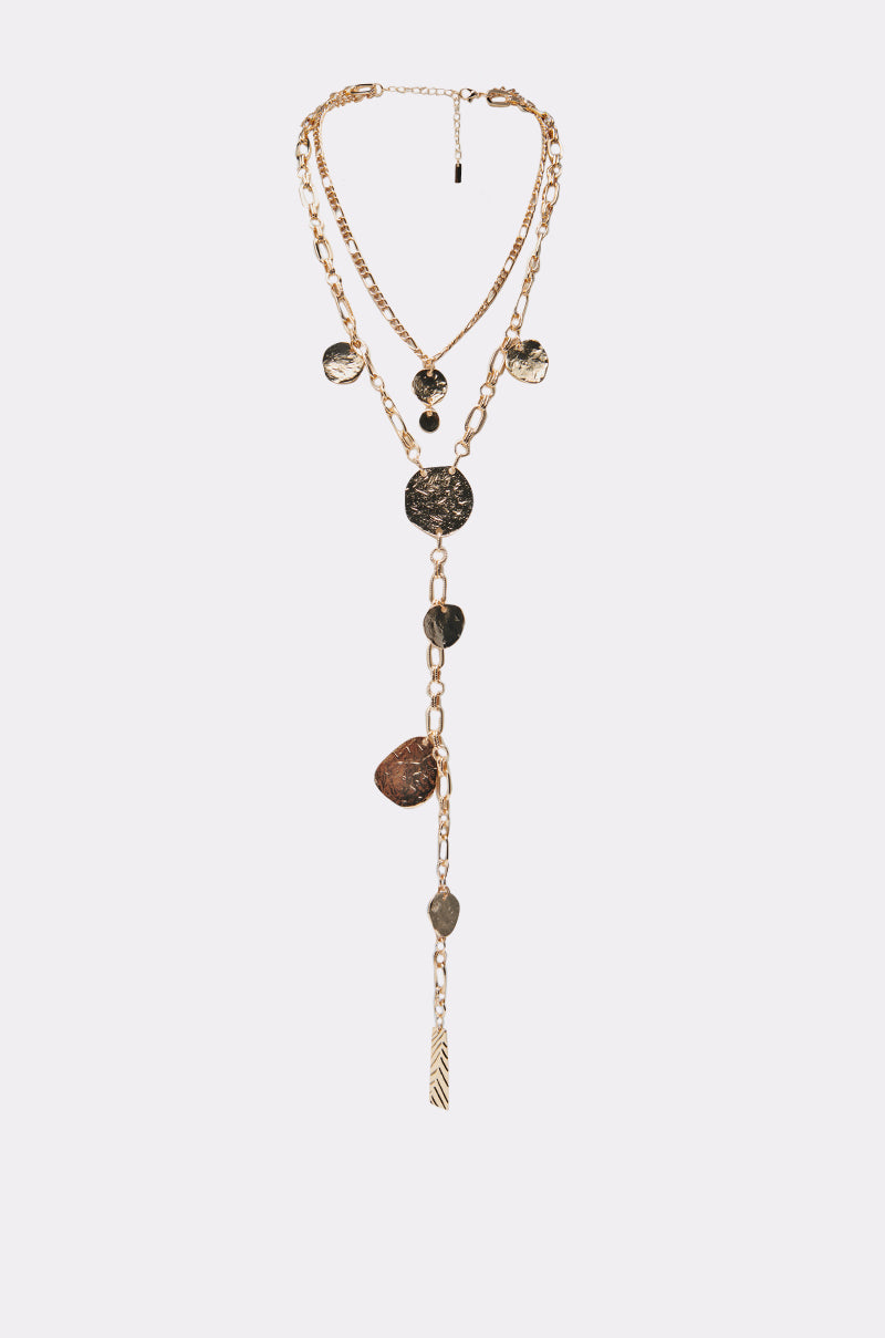 The HERE FOR THE VIBES NECKLACE features layered gold chains, textured metallic coin pendants, and a Y-shaped drop finished with a leaf charm, showcased on a simple light background. 0