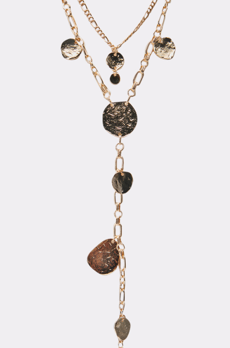 The HERE FOR THE VIBES NECKLACE showcases a gold chain with multiple hammered, irregular round and oval pendants at varying lengths for a layered, textured style. Photographed on a plain white background. 2