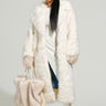 A person draped in a maxi-length silhouette is wearing the TOASTED MARSHMALLOW FUR COAT, along with a matching hat and large faux fur bag. They are stylishly accessorized with sunglasses, white boots, and hoop earrings, standing against a plain background.