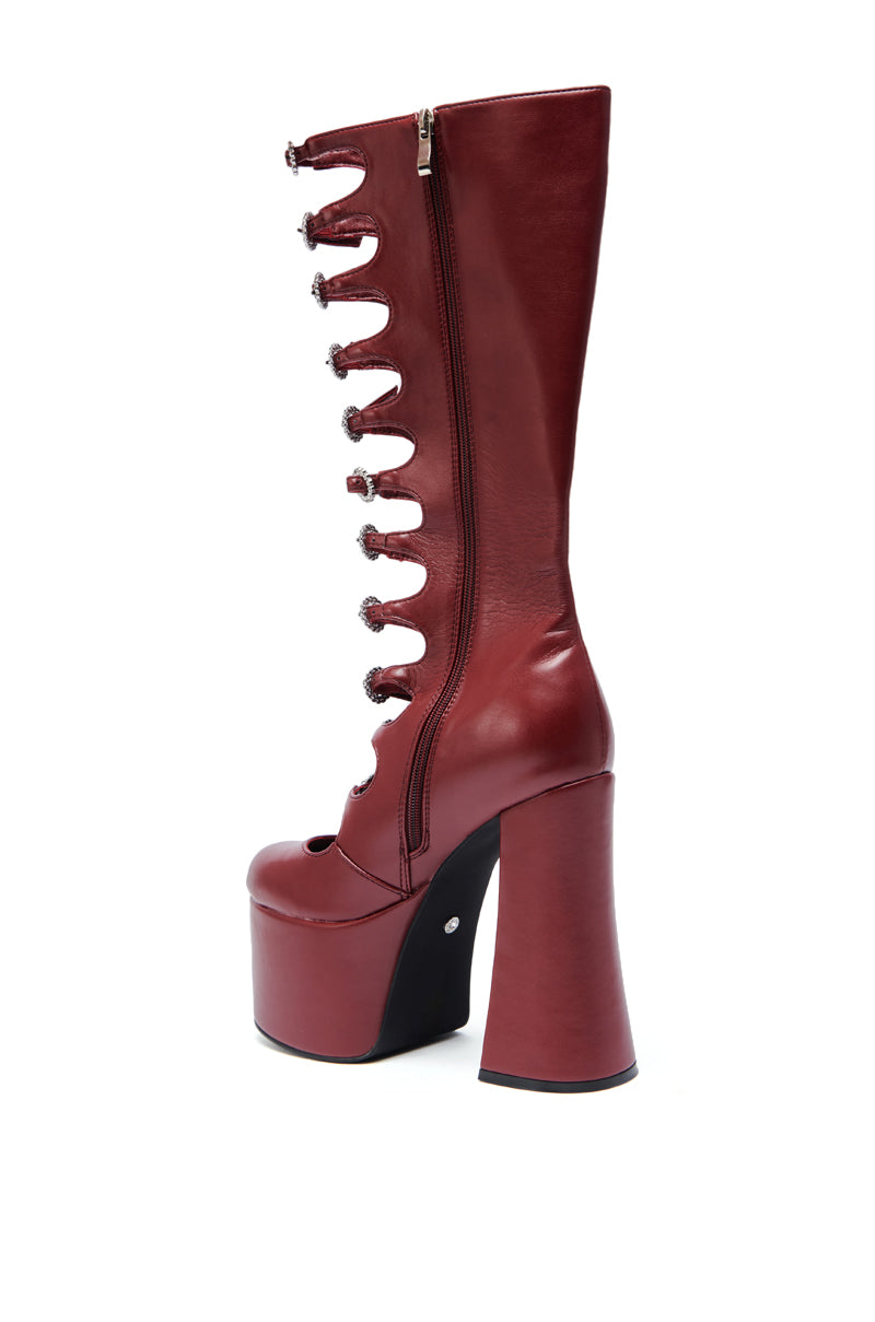 The AZALEA WANG TOMLIN BURGUNDY PLATFORM BOOT is a shiny faux leather, high-heeled boot with a unique side cutout, decorative fastenings, side zipper, chunky heel, and mid-calf length.