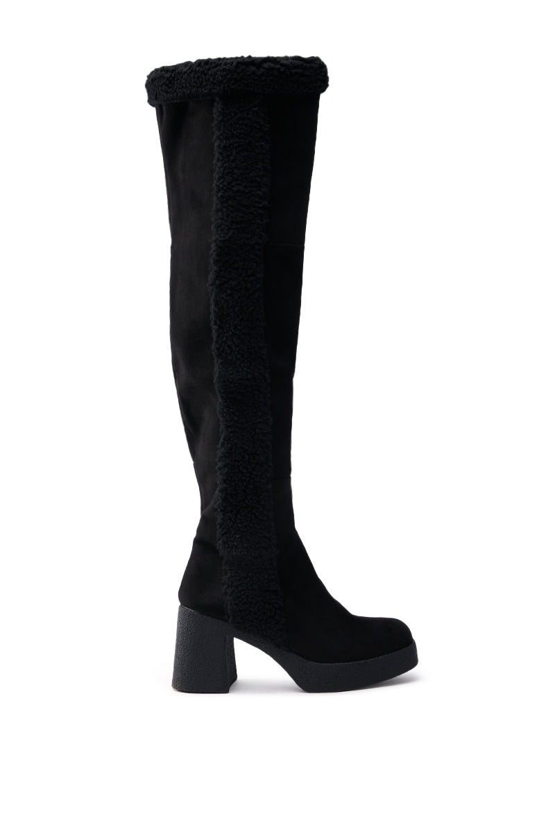 The TOP TIER BLACK CHUNKY BOOT is a knee-high boot with plush trim and panel, featuring a chunky heel. Made of faux suede, it offers a sleek and stylish look.