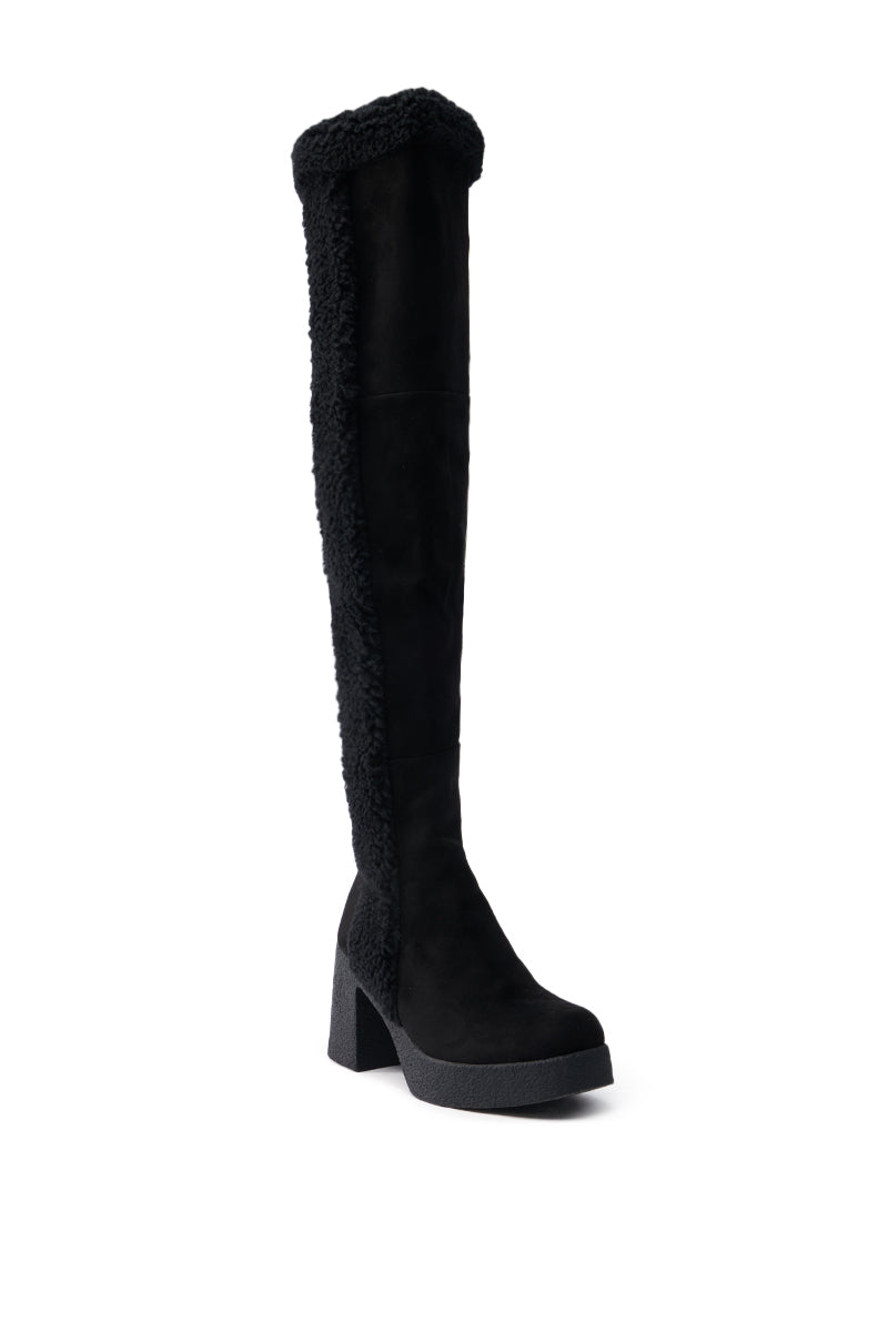 The TOP TIER BLACK CHUNKY BOOT is a tall thigh-high boot with a chunky heel, featuring faux shearling trim along the sides and top. Made from faux suede, it combines style with cozy comfort.