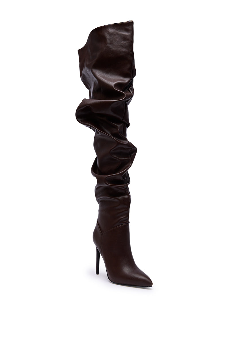 The AZALEA WANG TORVIS Chocolate Slouchy Over The Knee Boot features a tall, dark brown, ruched shaft, pointed toe, and sleek stiletto heel, standing upright against a plain white background.