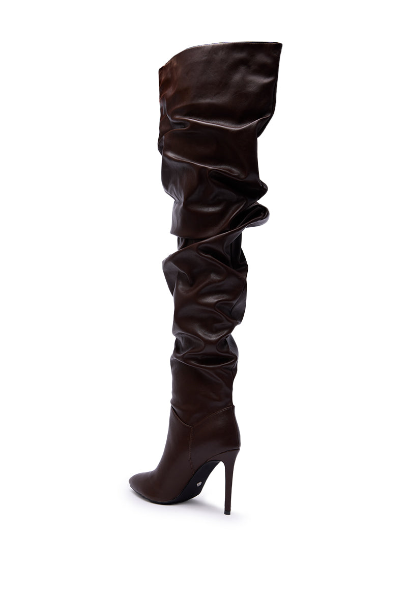 The AZALEA WANG TORVIS CHOCOLATE SLOUCHY OVER THE KNEE BOOT is a dark brown faux leather boot with a pointed toe, stiletto heel, and ruched shaft, shown against a white background.