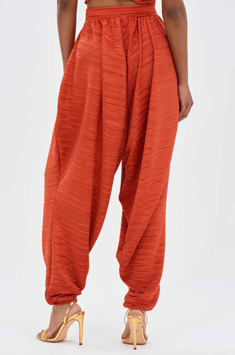 A person stands with their back to the camera against a plain white background, wearing textured, loose-fitting MAYAH WIDE LEG PLISSE PANT IN RED and yellow high-heeled sandals for a touch of AKIRA Label Mayah style. 3