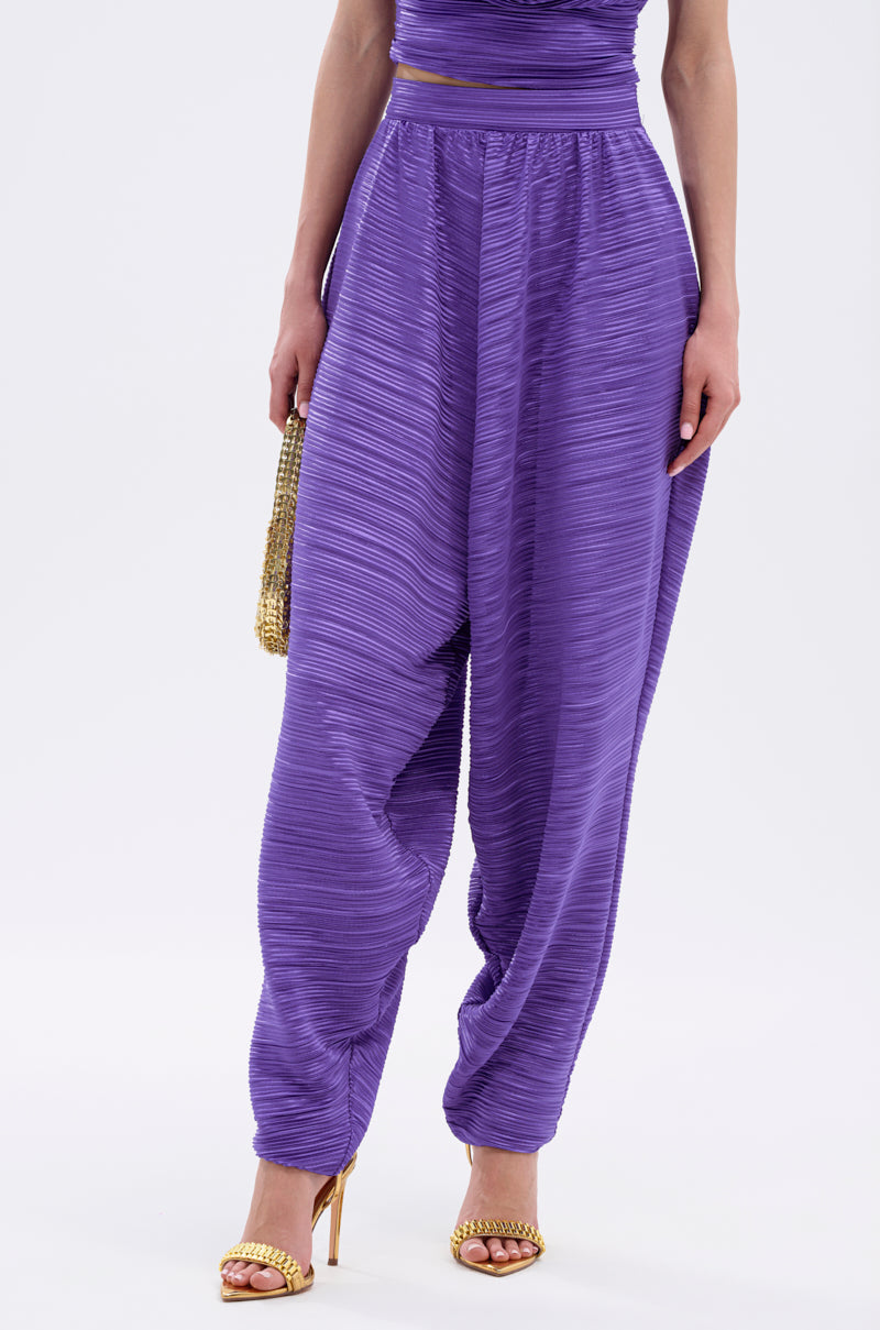 A person wears the MAYAH WIDE LEG PLISSE PANT IN PURPLE with a matching top, gold strappy heels, and a small gold clutch against a plain white background. 2