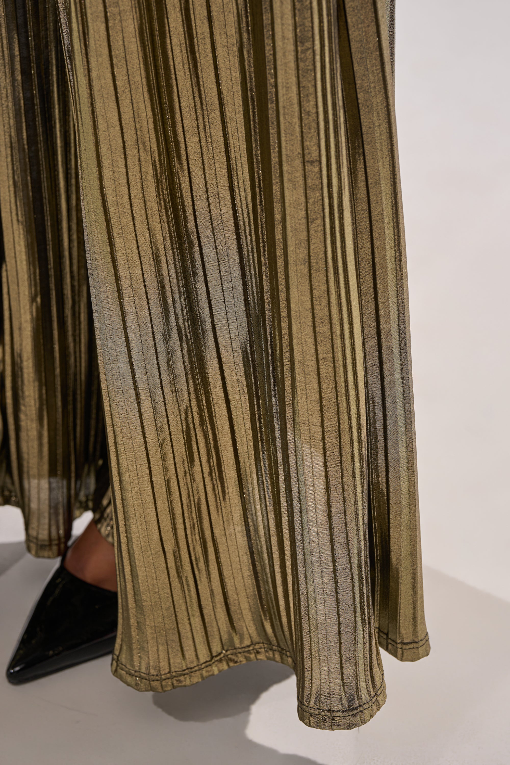 A close-up of the BEST DRESSED PALAZZO PANT, featuring metallic pleats and wide legs, styled with black pointed-toe shoes against a light background. 9