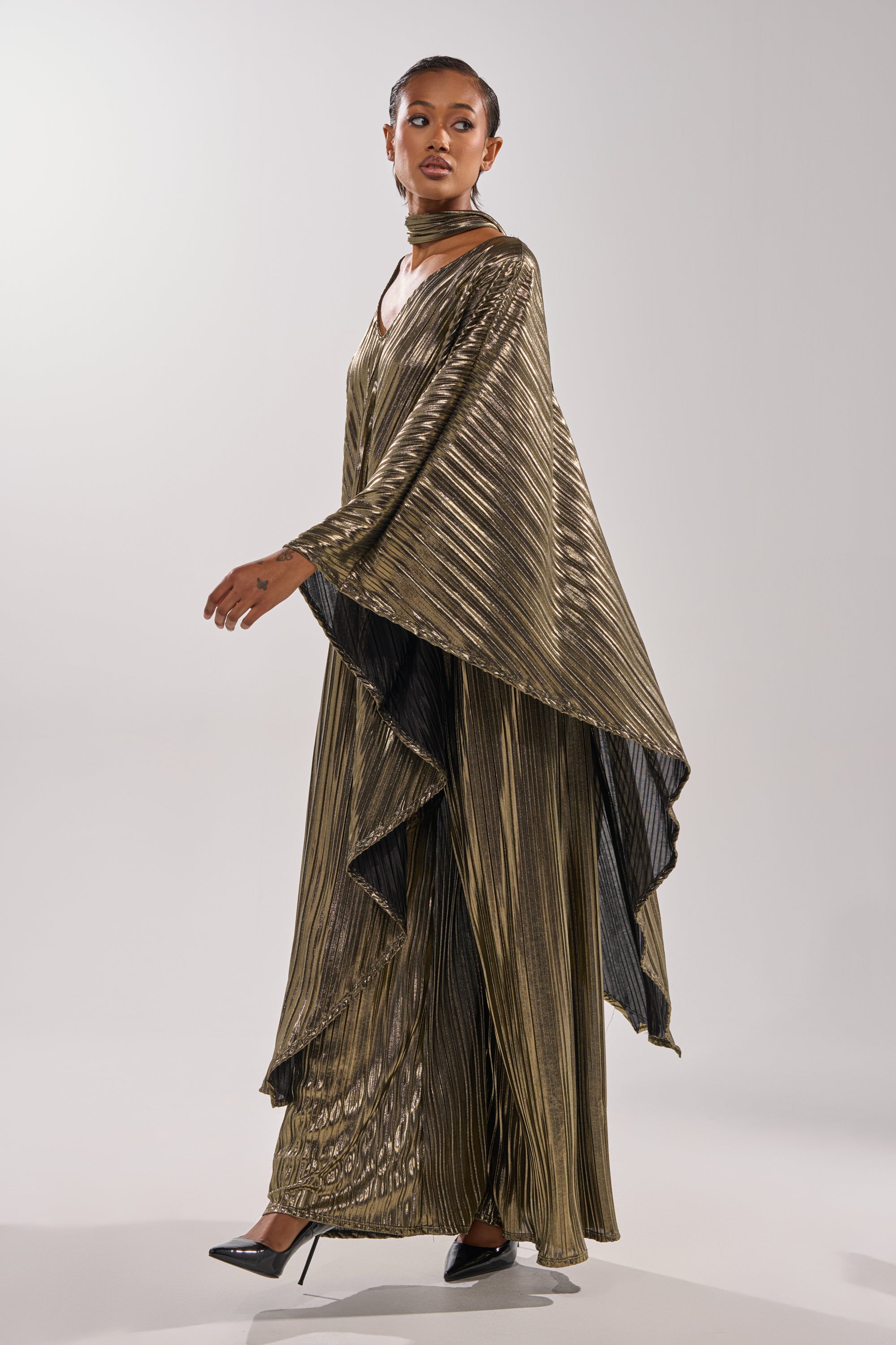 A woman models the BEST DRESSED BLOUSE in a studio, styled with high heels and a dramatic cape—an elegant look against a plain backdrop. 10