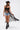A woman wears the SEE YOU LATER LACE BLOUSE under a black sleeveless duster, paired with a black cowboy hat, denim shorts, and black boots with silver fringe, walking confidently against a plain white background.