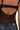Close-up of a person’s back in the SEE YOU LATER LACE BLOUSE, featuring sheer lace, cut-out detail, and adjustable straps, paired with blue denim jeans. The delicate fabric reveals the skin for an eye-catching statement look.