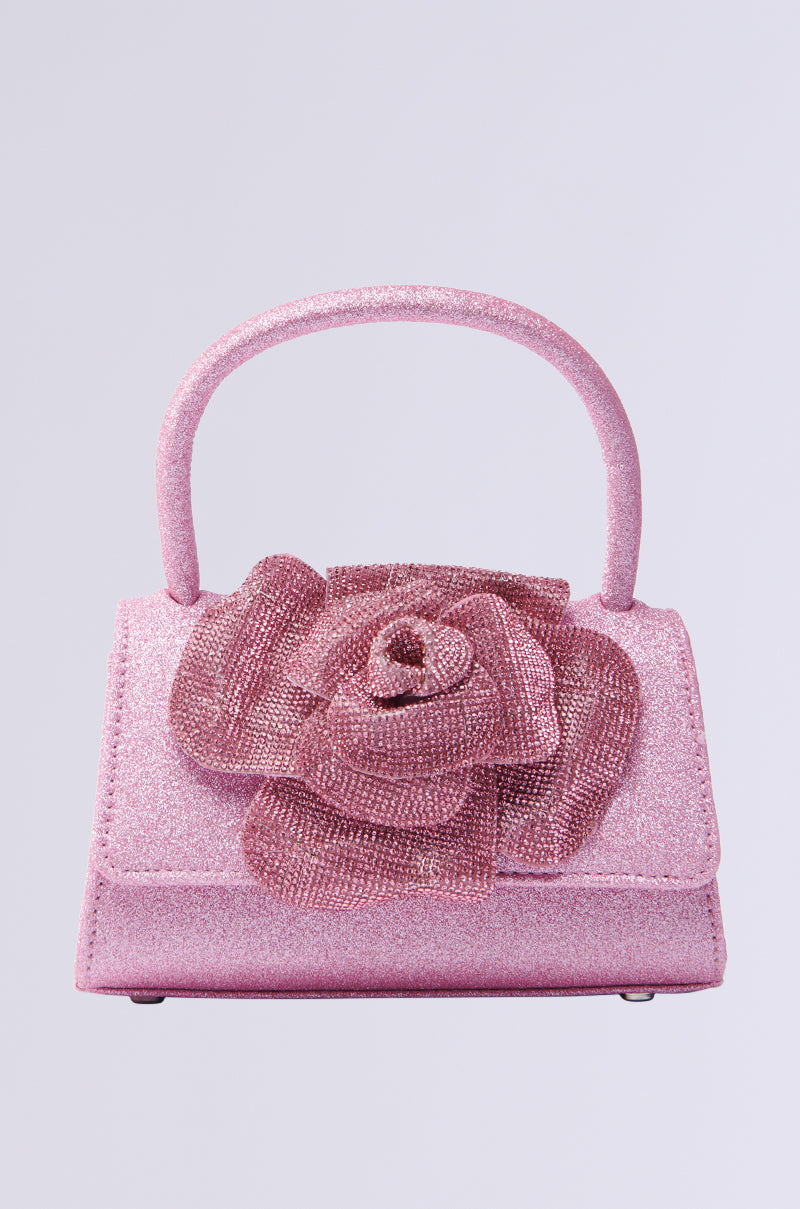 The DANCE ALL NIGHT FLORAL MINI BAG is a sparkly pink floral mini bag with a single top handle and a large decorative rose on the front. Its textured, glittery surface shines like rhinestones against a plain light background, offering an elegant crossbody fit for versatile styling.
