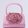 The DANCE ALL NIGHT FLORAL MINI BAG is a sparkly pink floral mini bag with a single top handle and a large decorative rose on the front. Its textured, glittery surface shines like rhinestones against a plain light background, offering an elegant crossbody fit for versatile styling.