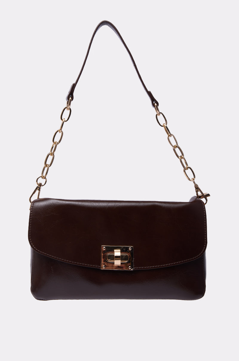 The BUTTER SOFT PURSE is a dark brown faux leather bag with a gold chain strap, leather accents, a rectangular flap, and a front gold-tone clasp closure, displayed against a plain white background. 4