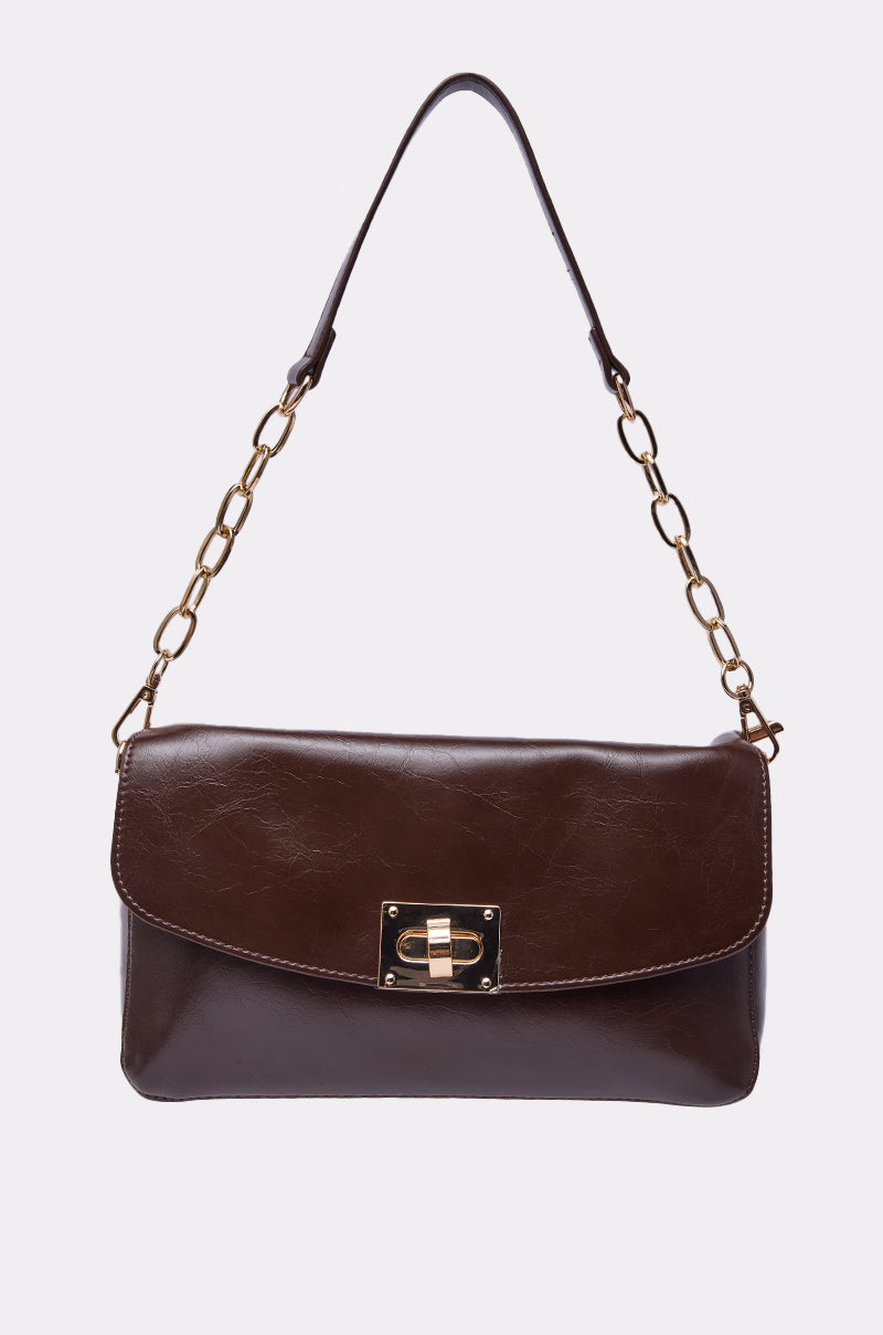 The BUTTER SOFT PURSE is dark brown with a gold front clasp and a shoulder strap featuring gold chain links. It is displayed against a plain, light-colored background. 1
