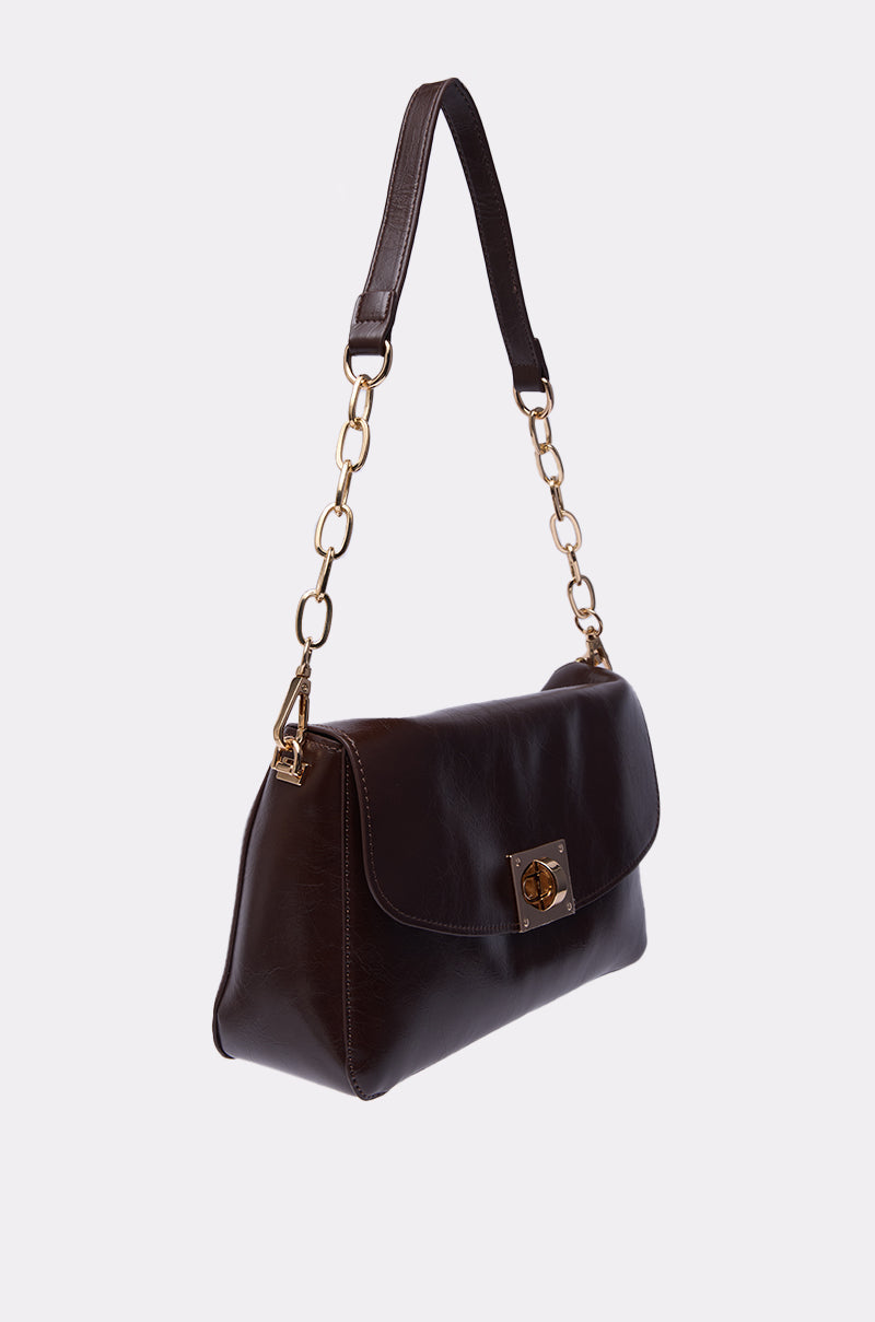 The BUTTER SOFT PURSE is a dark brown faux leather shoulder bag with a gold chain strap, leather handle, and flap closure with a gold turn-lock clasp, shown against a plain white background. 5